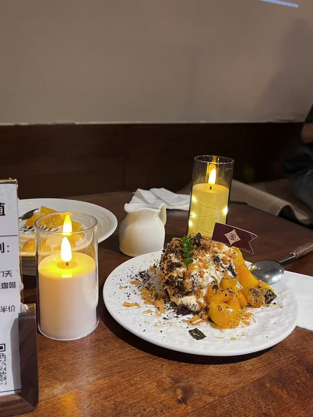 Glass-enclosed LED candles beside a plated dessert on a wooden café table
